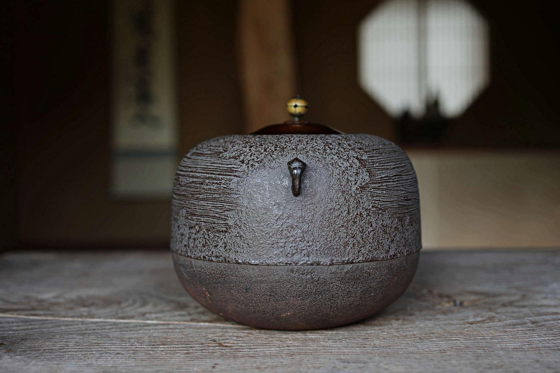 A dark brown ceramic teapot with a small handle and a small yellow ball on top, sitting on a wooden surface.