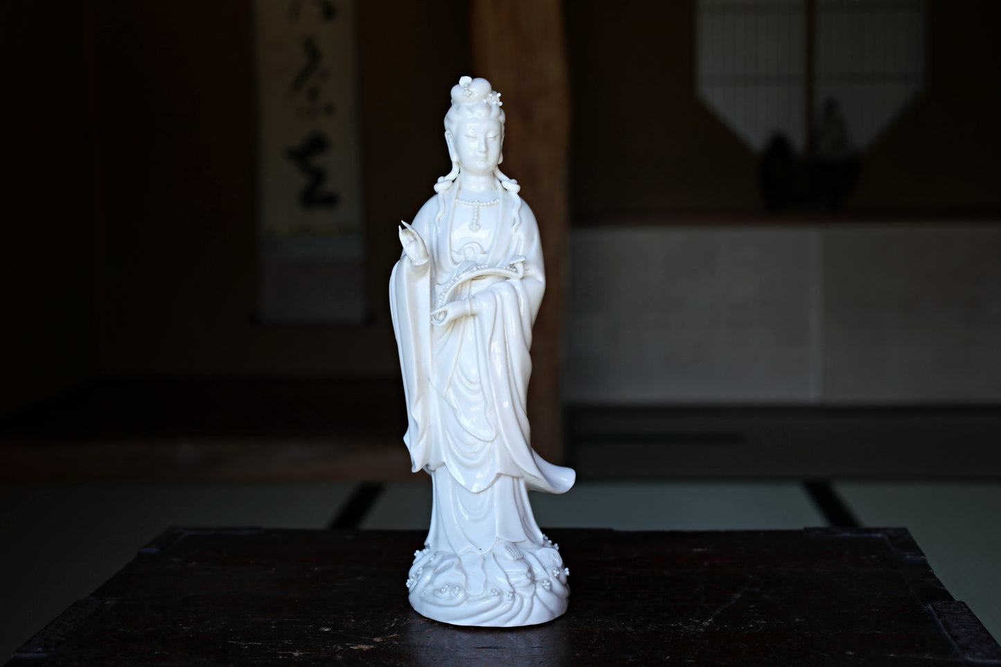 A white ceramic statue of a deity, possibly a Buddha, is displayed on a wooden surface.