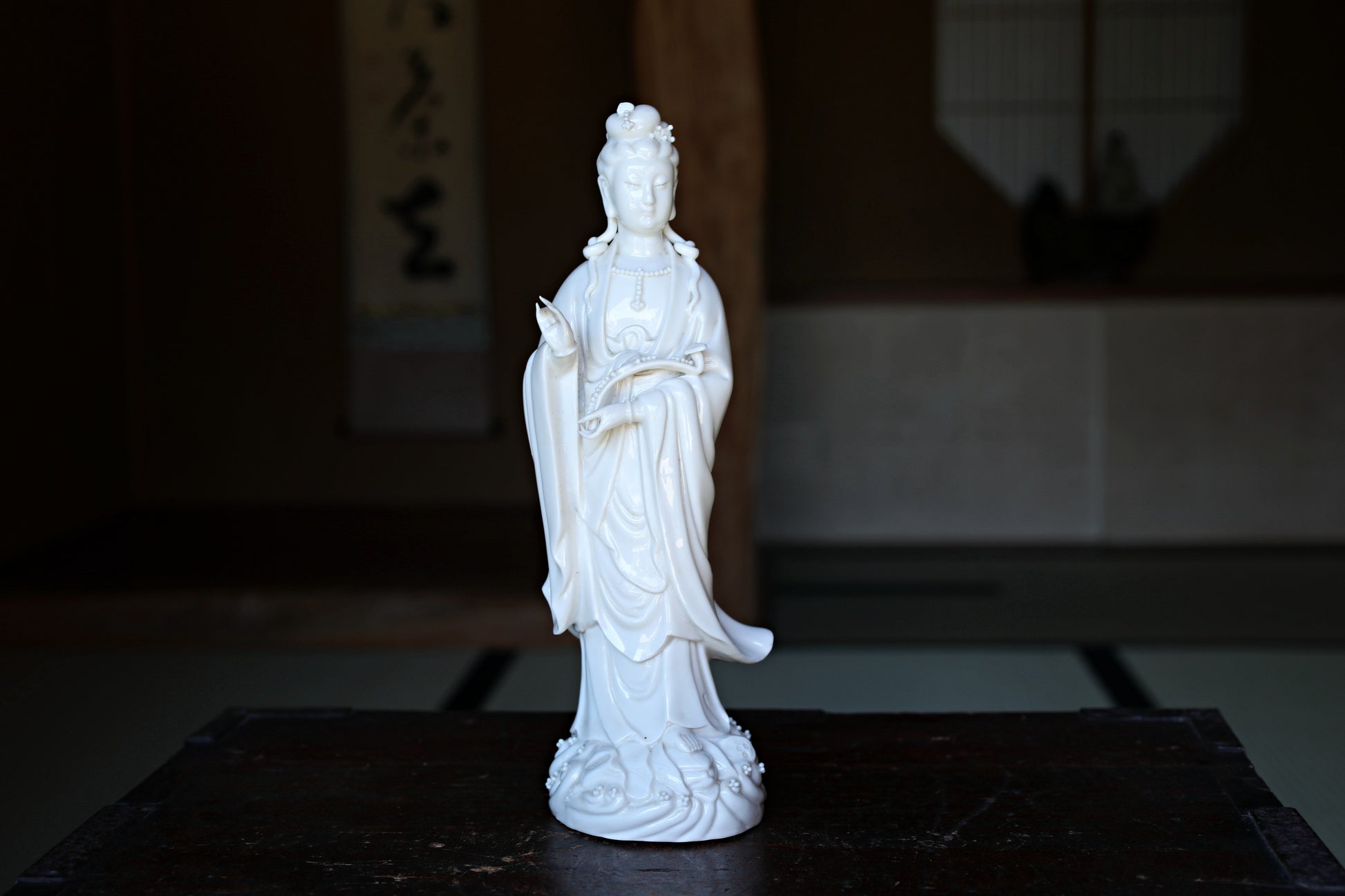 A white ceramic statue of a deity, possibly a Buddha, is displayed on a wooden surface.