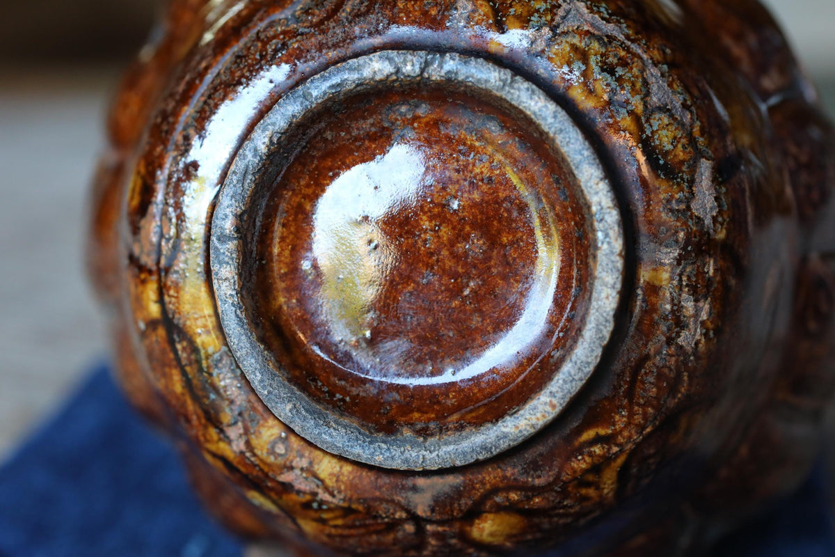 A close-up view of a ceramic vase with a brown and orange patterned surface, featuring a central circular opening.