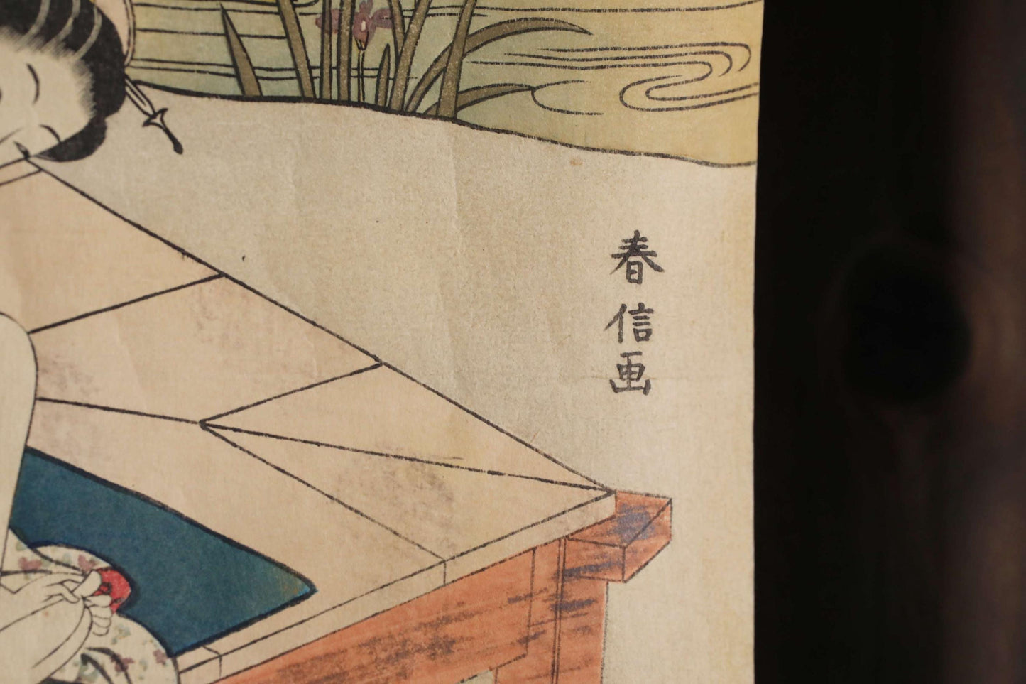 The image is a close-up of a painting or artwork, featuring a woman sitting at a table with a blue cushion. The artwork is in Japanese, and there is some text in the image.