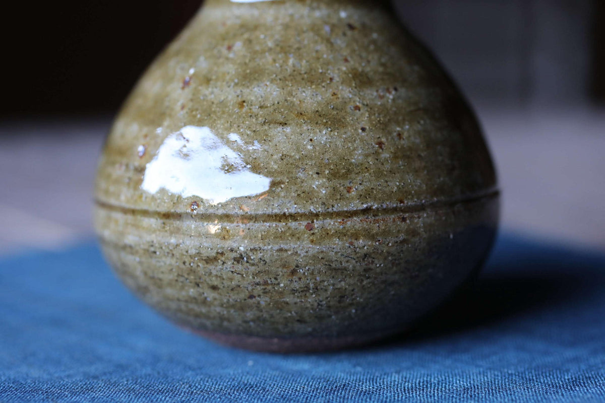 A close-up image of a ceramic vase with a speckled, speckled texture, resting on a blue surface.