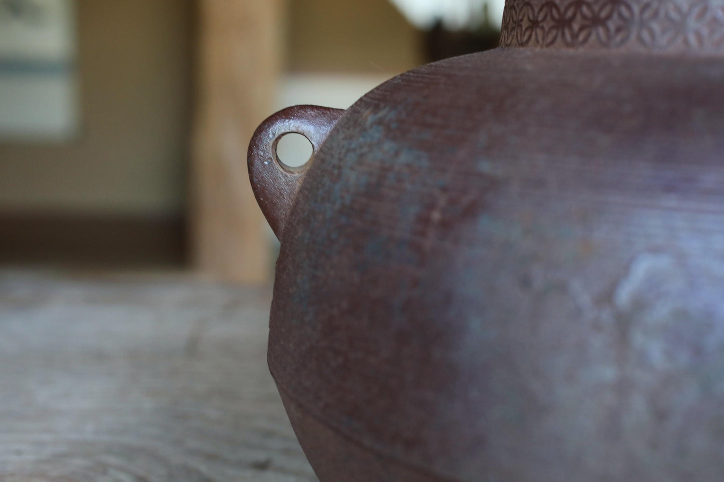 A close-up view of a dark-colored ceramic vase or container with a metallic sheen, sitting on a wooden surface.