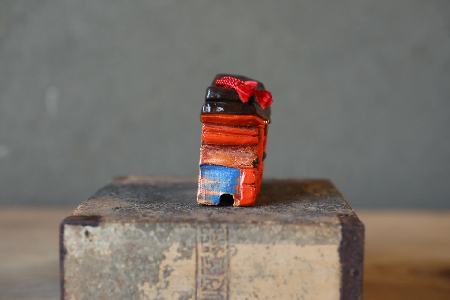 A small, colorful object with a red bow on top, sitting on a wooden surface against a gray background.