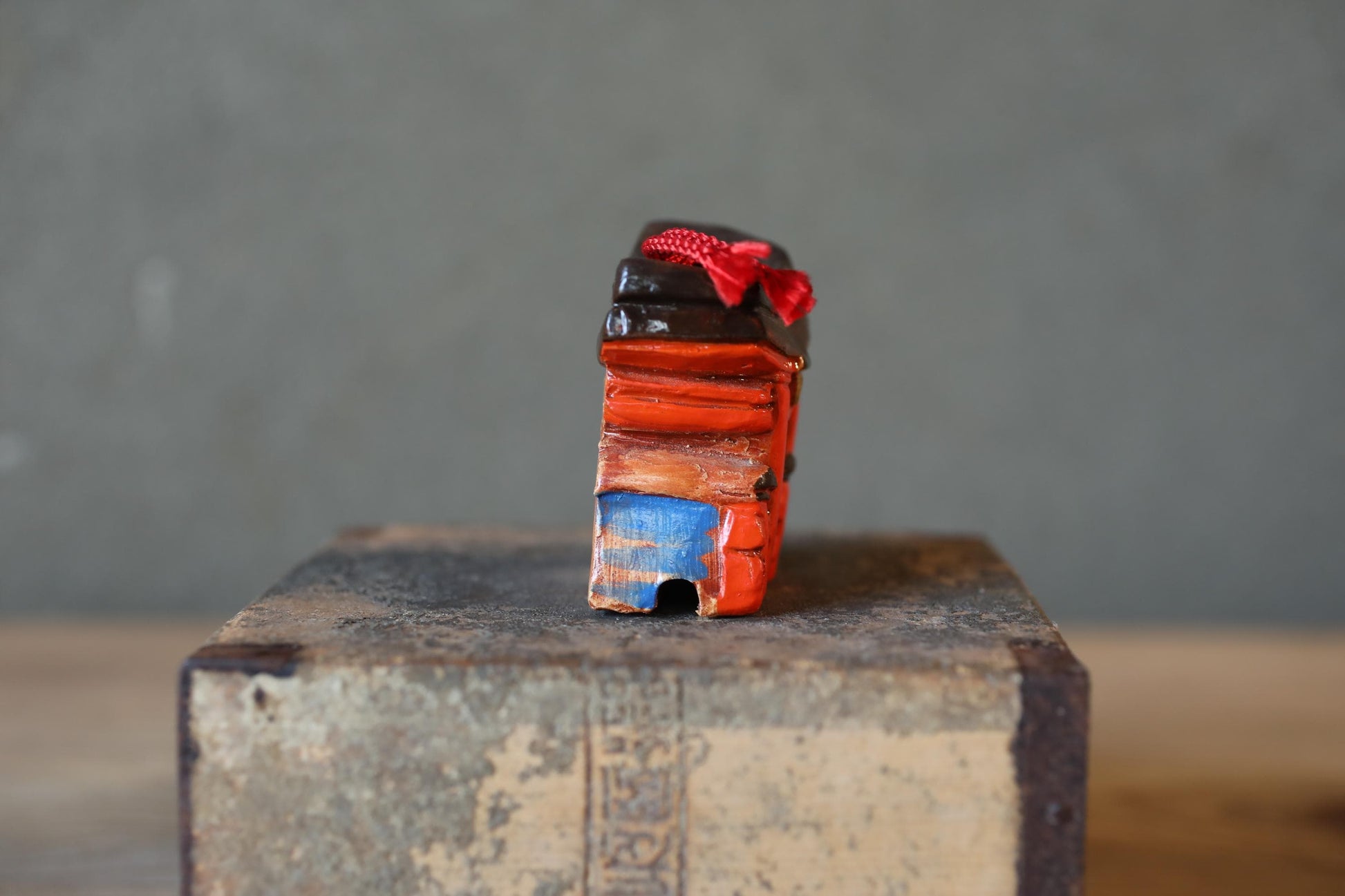 A small, colorful object with a red bow on top, sitting on a wooden surface against a gray background.
