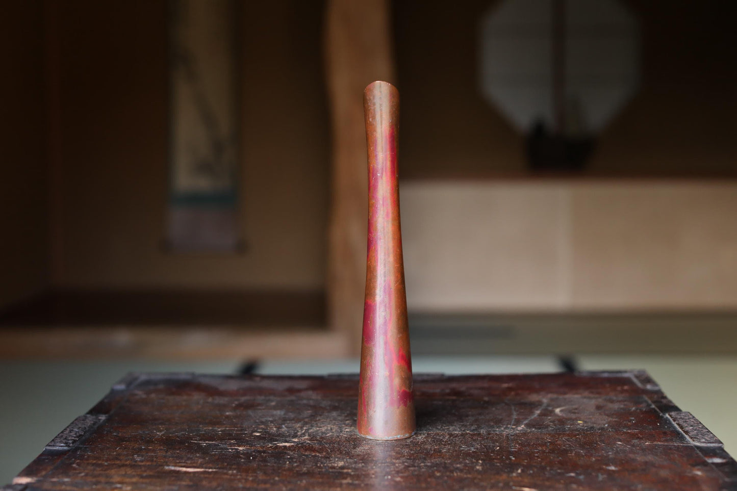 A tall, narrow, and shiny object with a reddish-brown hue is placed on a wooden surface.