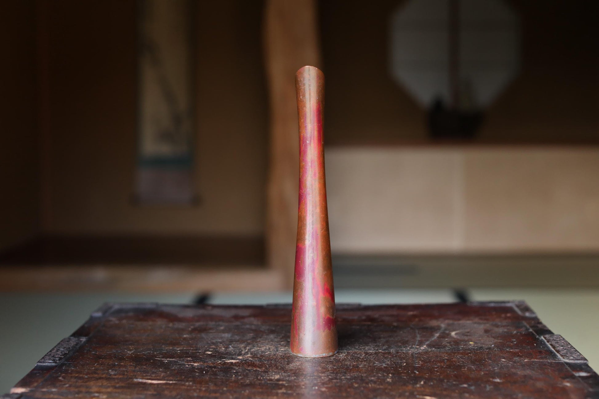 A tall, narrow, and shiny object with a reddish-brown hue is placed on a wooden surface.