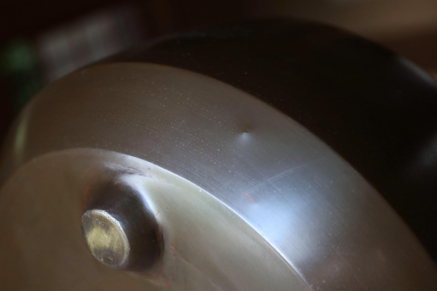 A close-up view of a metal surface with a small dent or scratch, and a small, round object on the surface.
