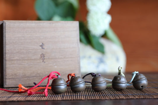 a wooden box with Japanese characters on it, along with a row of metal bells hanging from a bamboo mat.