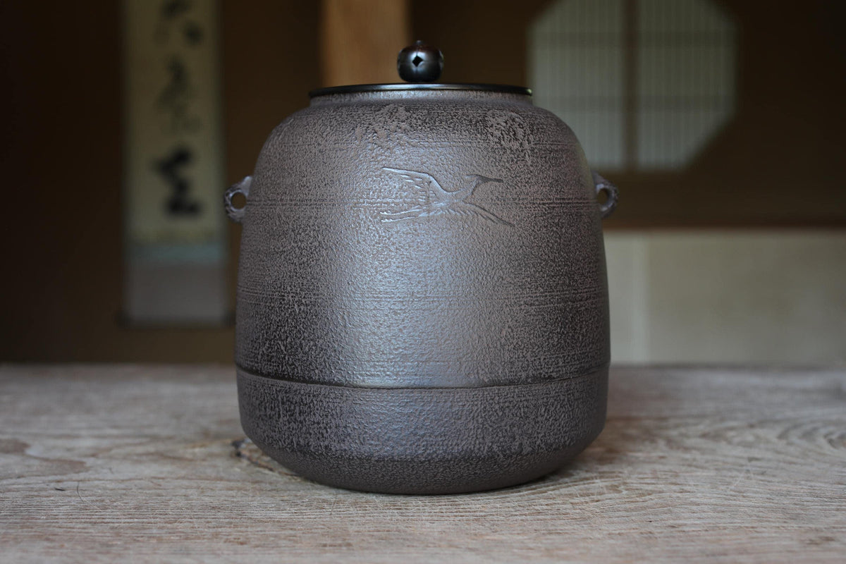 A black ceramic teapot with a bird design on it, sitting on a wooden surface.