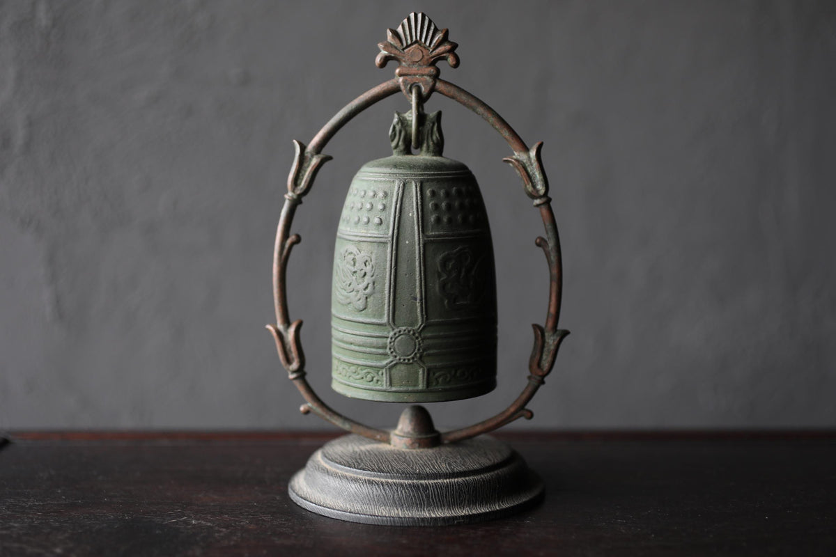 A green metal bell with a decorative metal frame is displayed on a dark surface.