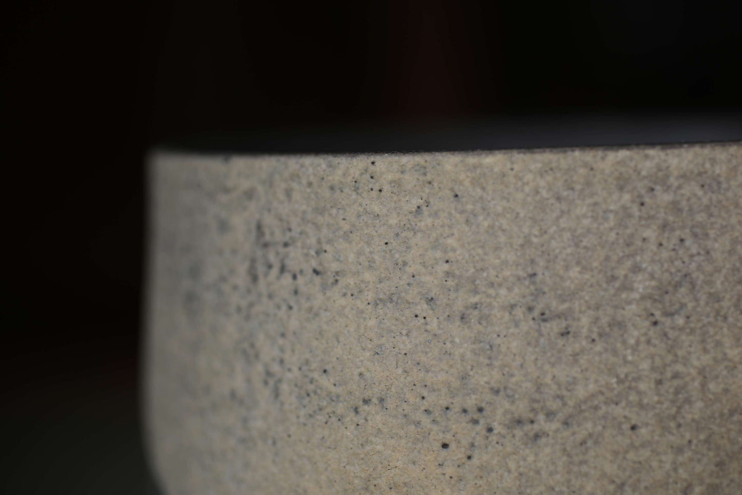A close-up view of a textured, speckled surface, possibly a piece of pottery or a ceramic object.