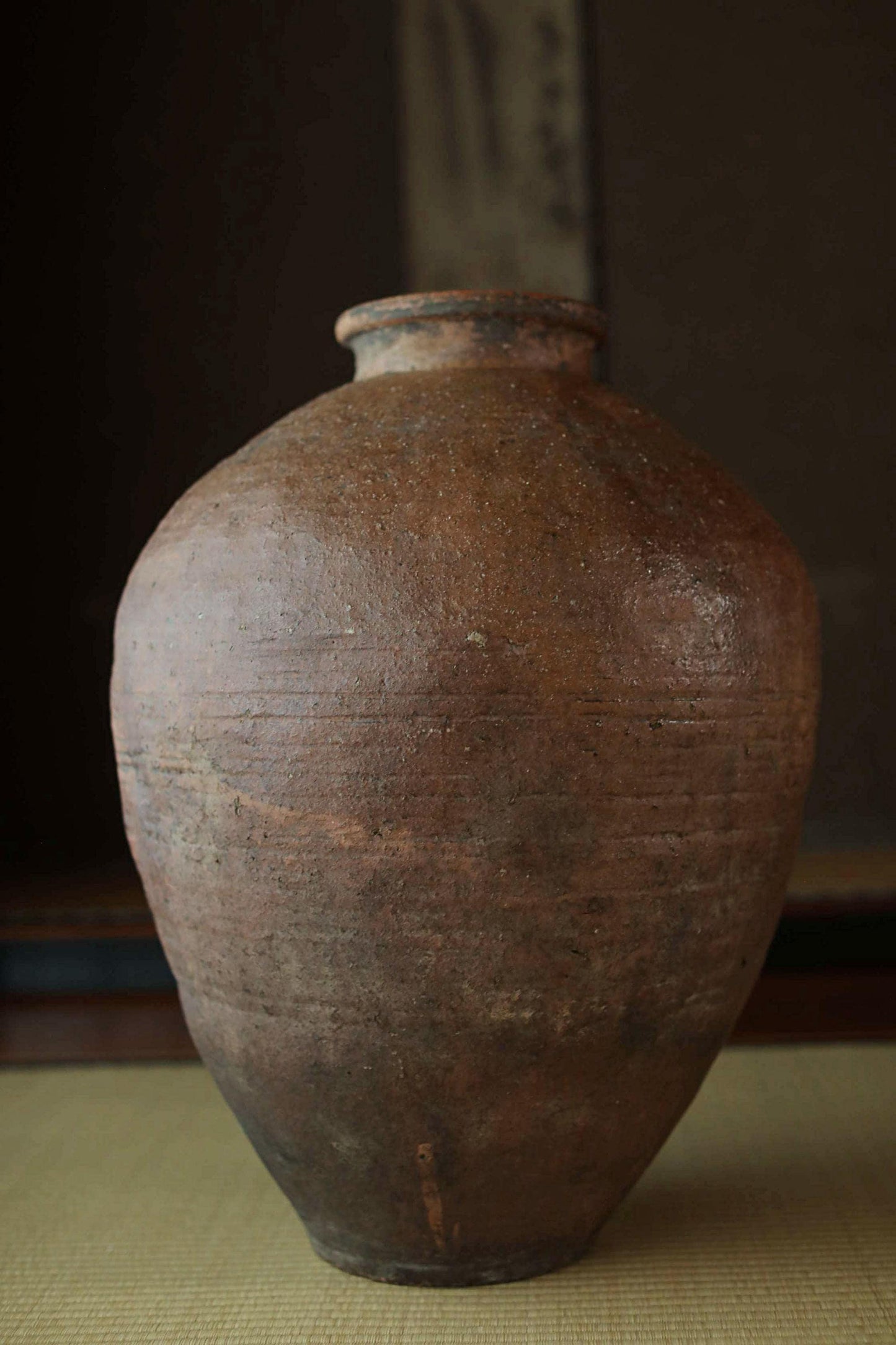 An old, large clay vase with a weathered, earthy appearance sits on a surface.