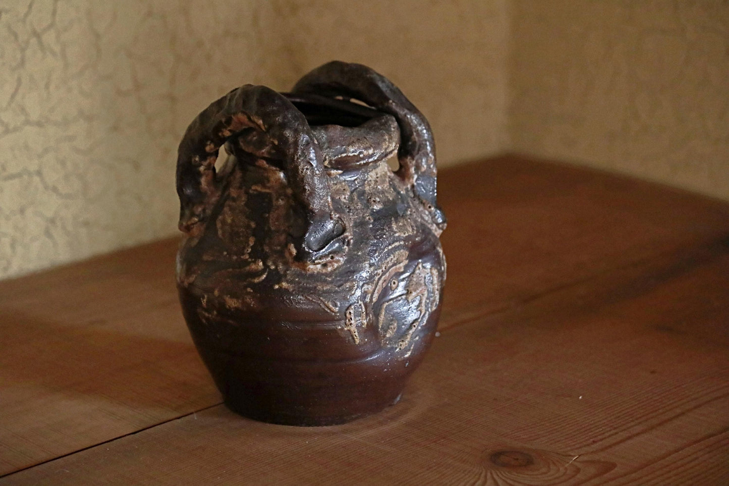 A dark brown ceramic vase with a unique, textured design sits on a wooden surface.
