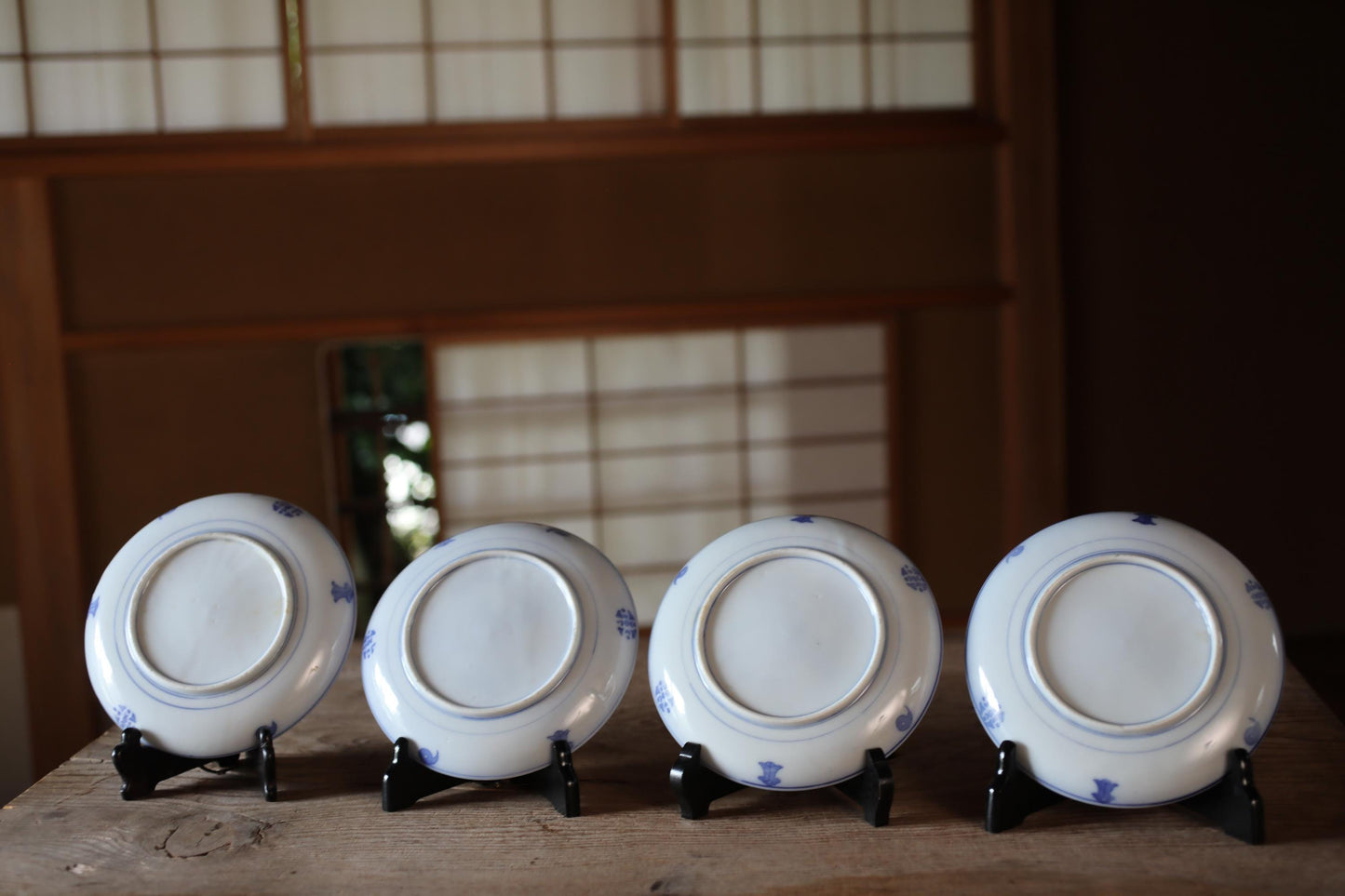 A row of four white plates with blue designs, each placed on a black stand, arranged on a wooden surface.