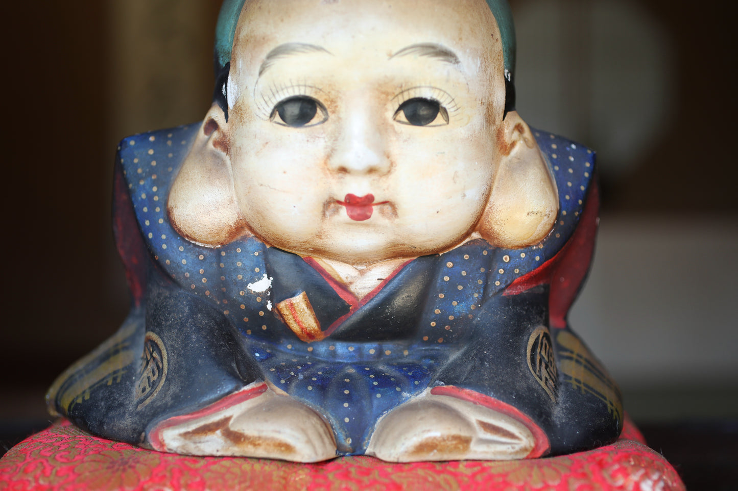 A close-up of a ceramic figurine depicting a young boy wearing a blue and red outfit with a red dot on the left side.