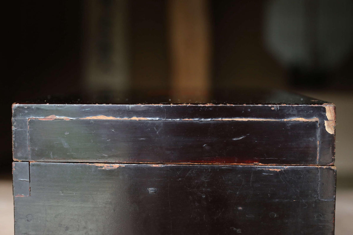 A close-up view of a black wooden box with visible signs of wear and tear, including peeling paint and visible cracks.