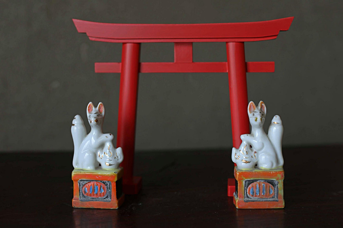 two ceramic fox statues positioned on either side of a red torii gate, which is a traditional Japanese gate used as a symbol of the entrance to a shrine.