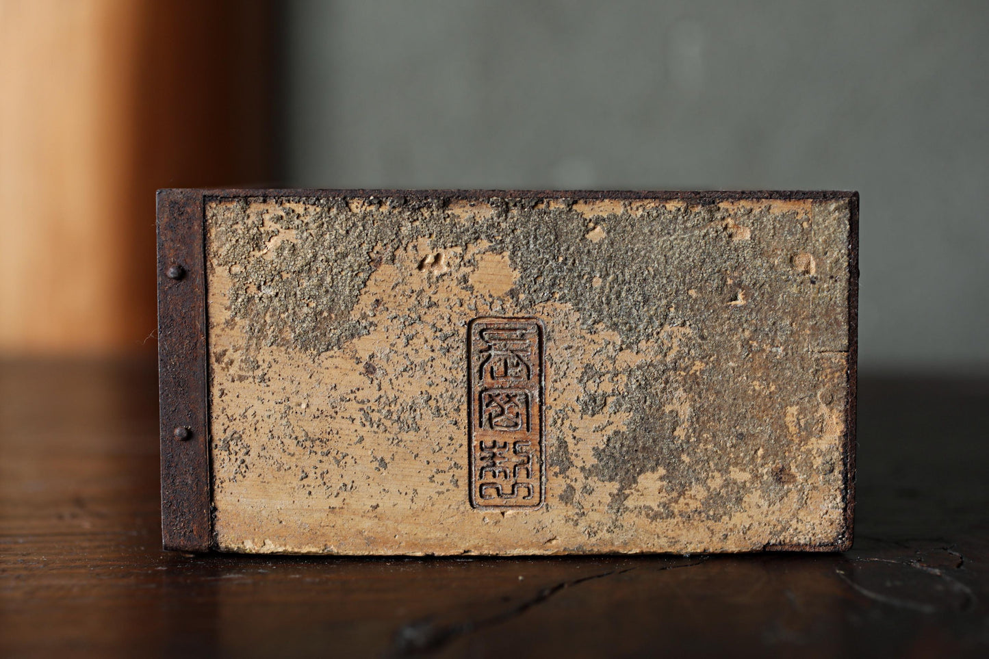 An old, weathered book or binder with a metal clasp and a faded, distressed appearance, sitting on a wooden surface.