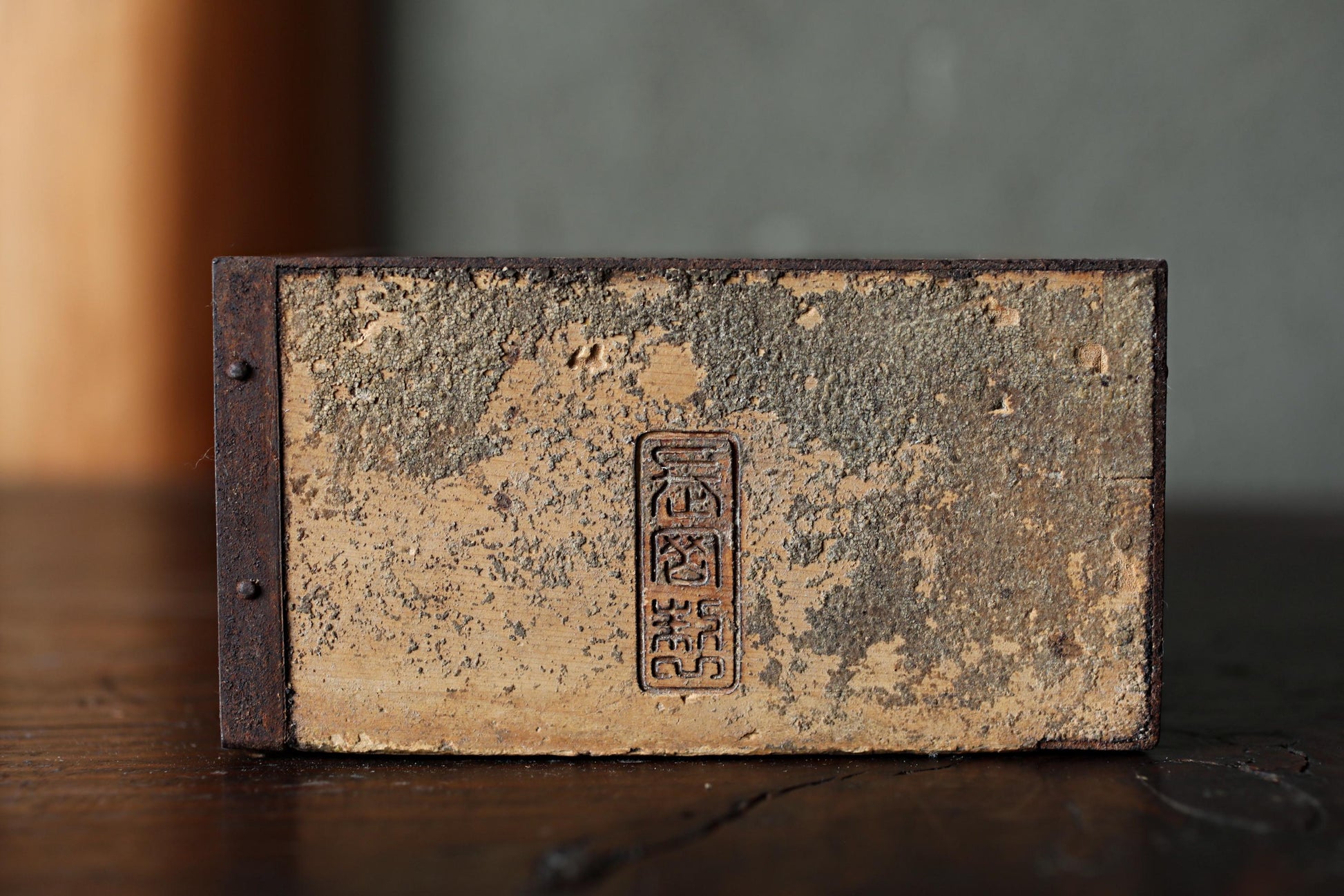 An old, weathered book or binder with a metal clasp and a faded, distressed appearance, sitting on a wooden surface.