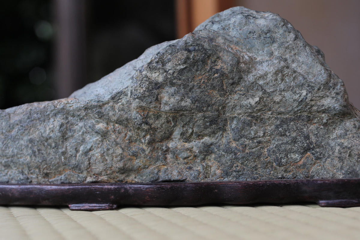 A large, gray rock sits on a dark wooden base, with a blurred background.