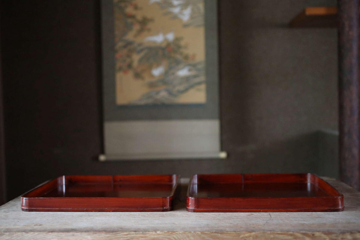 two wooden trays placed on a wooden surface, with a painting hanging on the wall in the background.