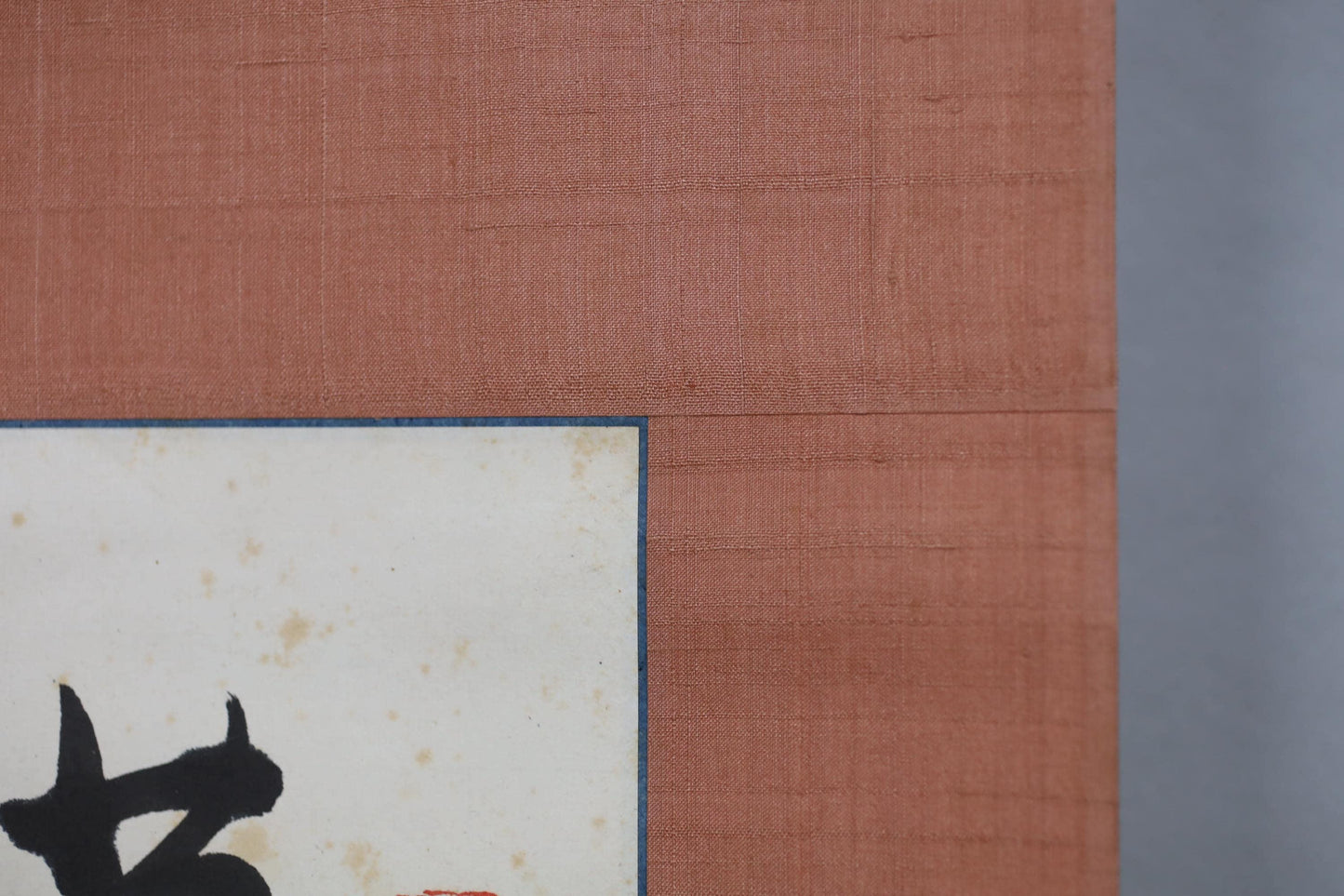The image is a close-up of a textured surface, possibly a piece of fabric or paper, with a black silhouette of a person or animal in the corner.