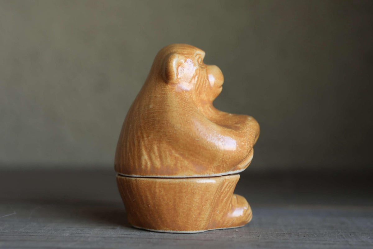 A ceramic monkey figurine sitting on a wooden surface.