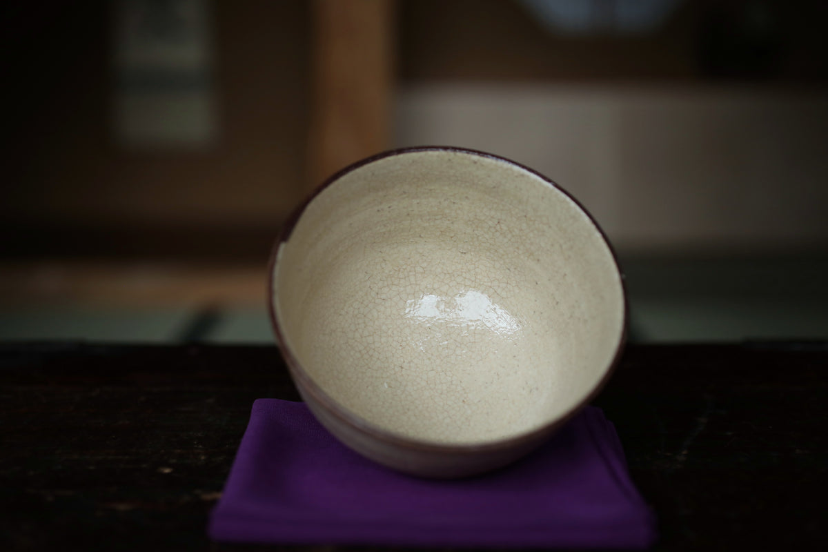 A white ceramic bowl with a dark rim sits on a purple cloth on a dark surface.