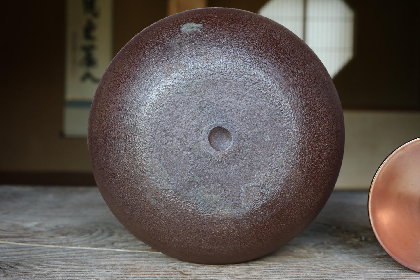 A close-up image of a dark brown ceramic bowl or vase with a hole in the center, placed on a wooden surface.