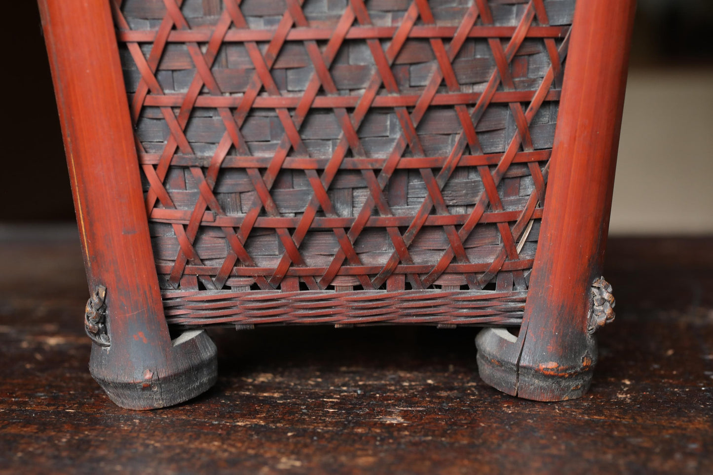 the back of a wooden basket with a woven pattern, featuring two wooden legs with a reddish-brown finish.