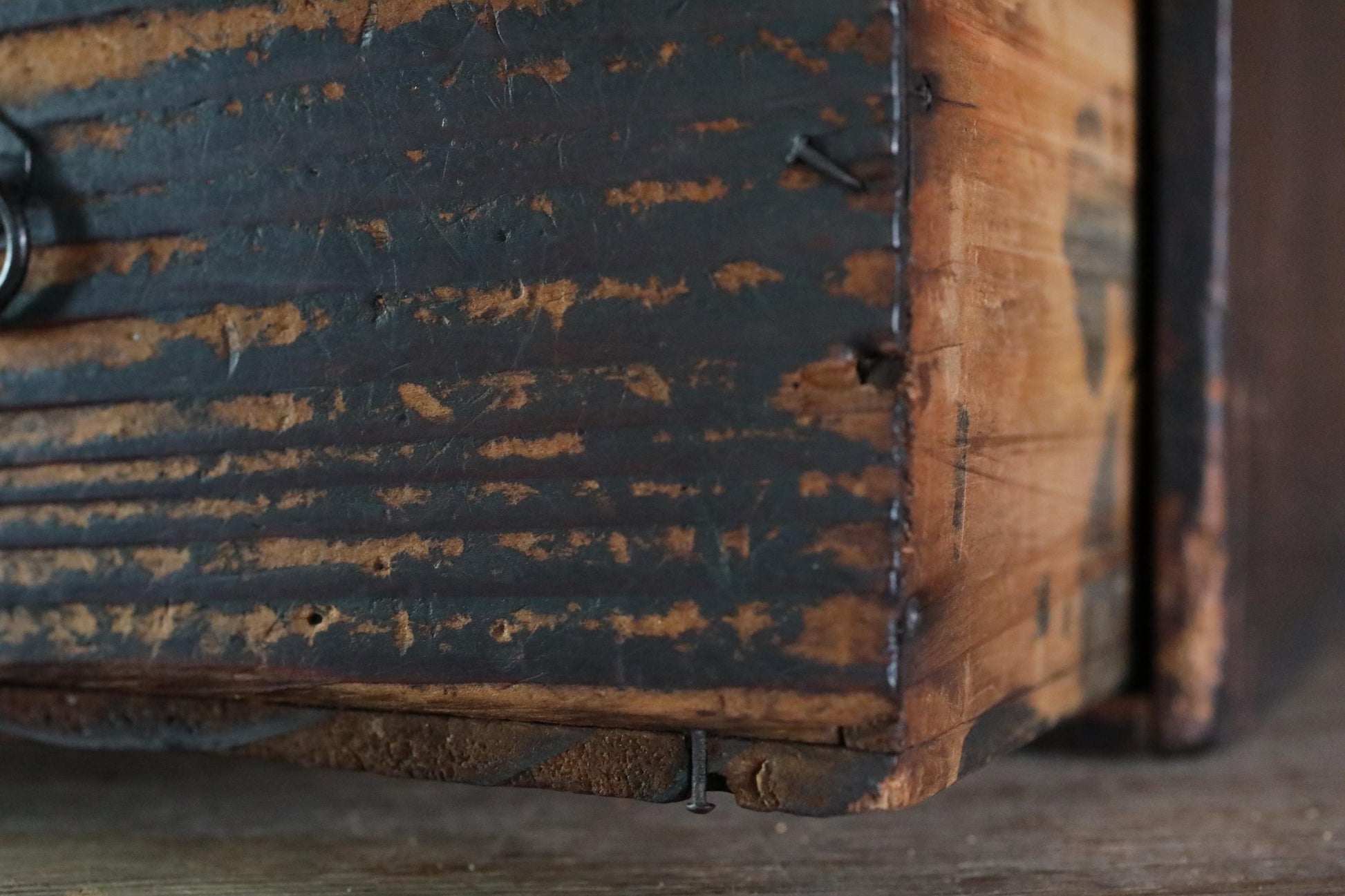 a close-up view of a weathered, wooden surface with a dark, distressed finish. The surface appears to be made of wood, with visible signs of wear and tear, such as peeling paint and cracks. The image does not contain any text or other discernible objects or actions.