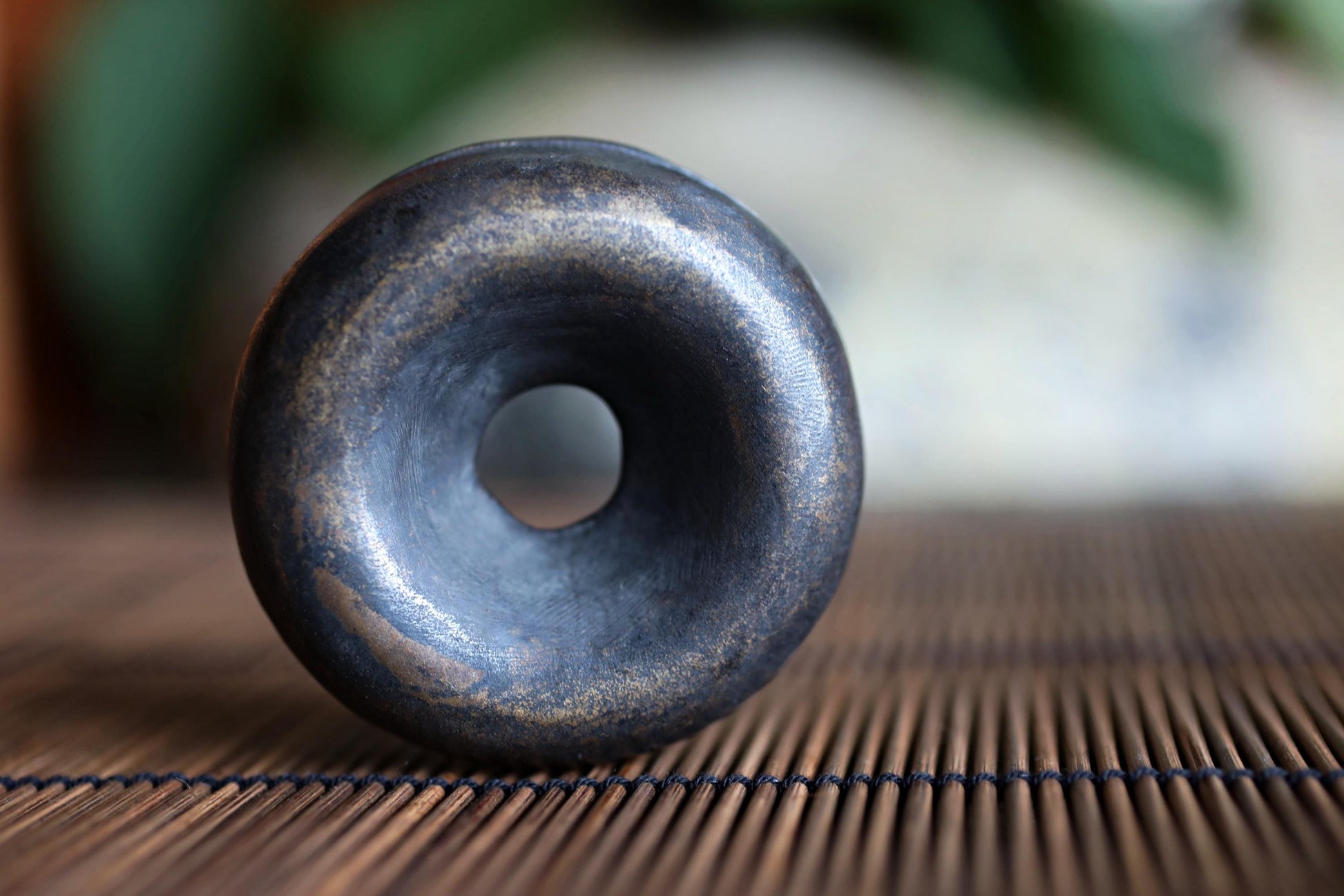 A close-up image of a black, circular object with a hole in the center, resting on a bamboo mat or placemat.