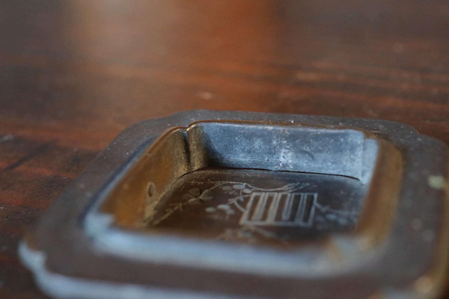 A close-up view of a metal ashtray on a wooden surface.