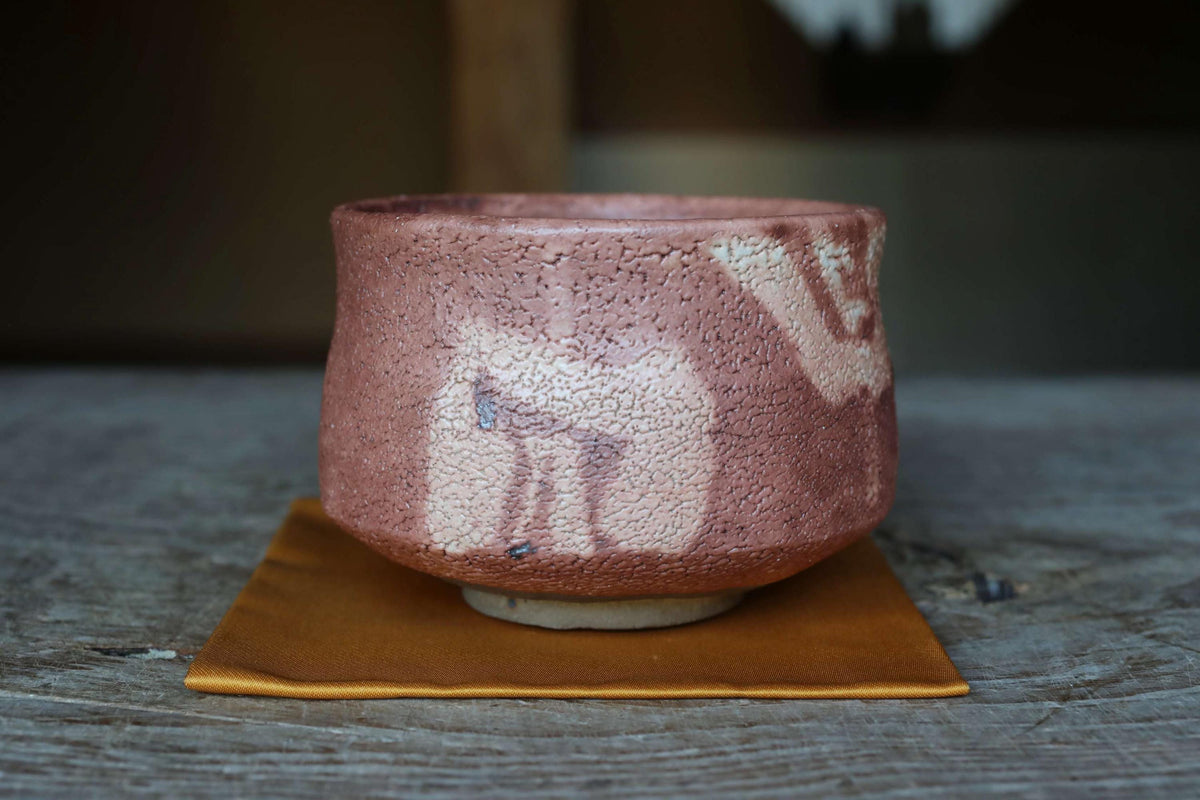 A ceramic teacup with a textured surface sits on a wooden surface, with a blurred background.