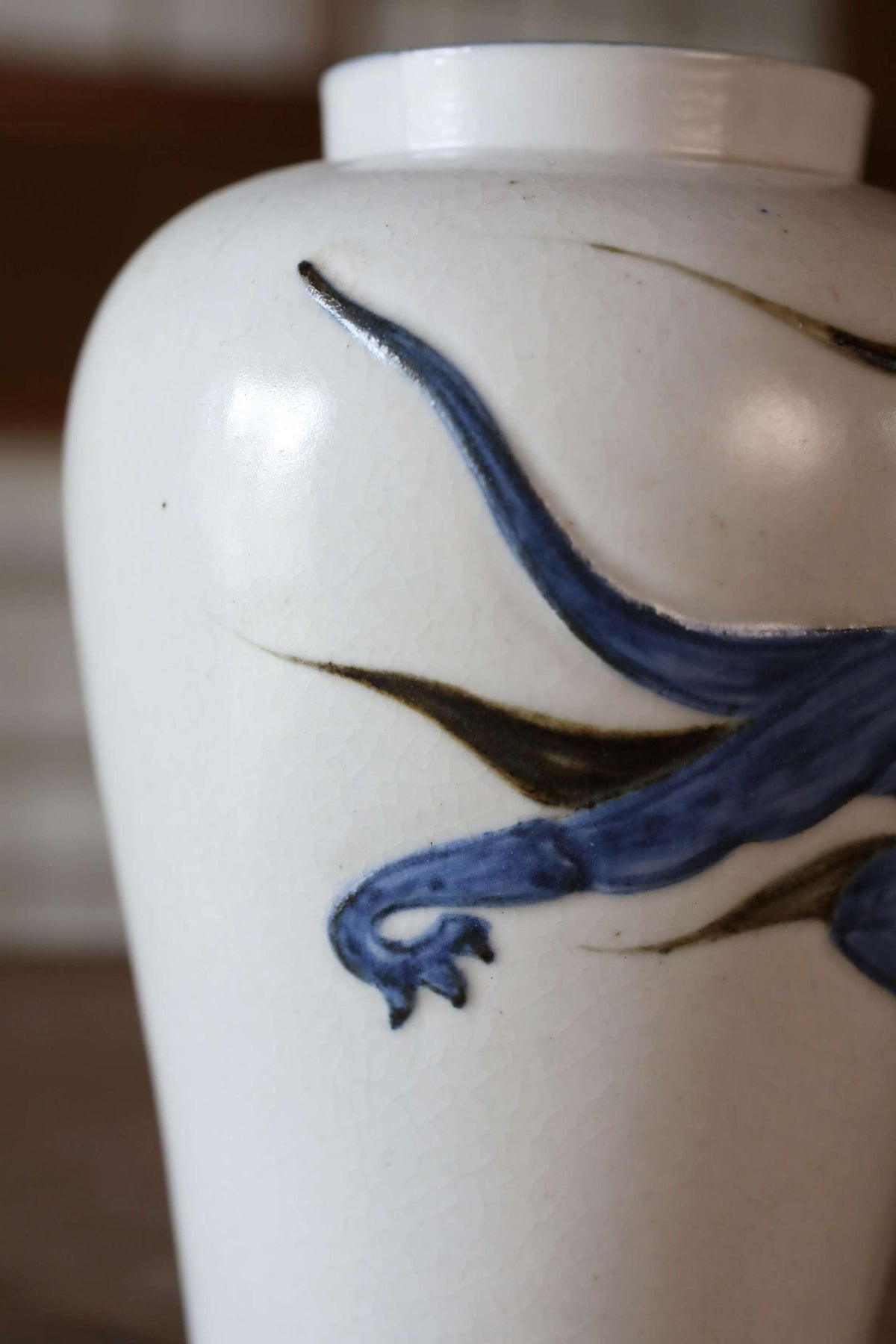 A close-up image of a white vase with a blue and black design depicting a stylized animal or creature.