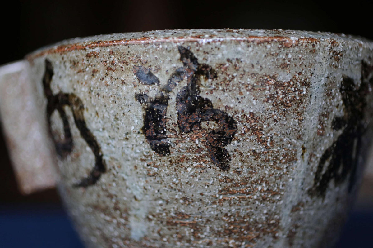 A close-up image of a ceramic mug or bowl with a textured surface and some black markings or designs.