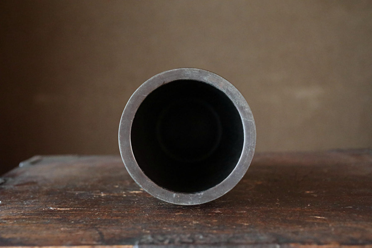 a black metal object, possibly a container or a piece of machinery, sitting on a wooden surface.