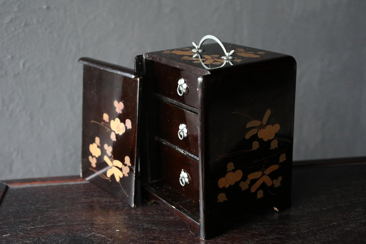 A dark brown wooden box with a handle and three drawers, decorated with a floral pattern.