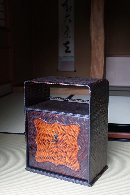 a dark brown wooden cabinet with an orange and black woven design on the front, placed on a tatami mat.