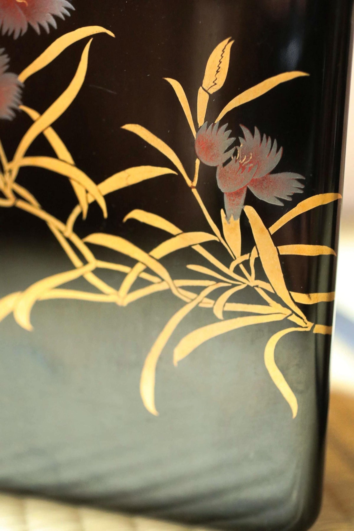 a close-up view of a black vase with a floral design on it. The design includes yellow leaves and a red flower, creating a visually appealing contrast against the black background.