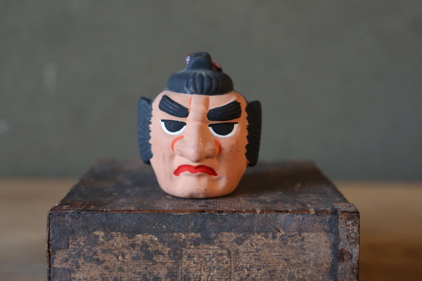 A toy figurine of a man with a stern expression is sitting on a wooden crate.