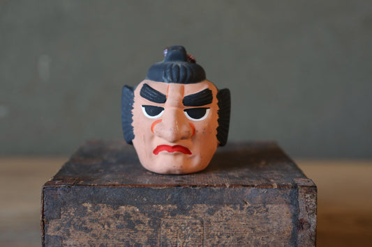 A toy figurine of a man with a stern expression is sitting on a wooden crate.