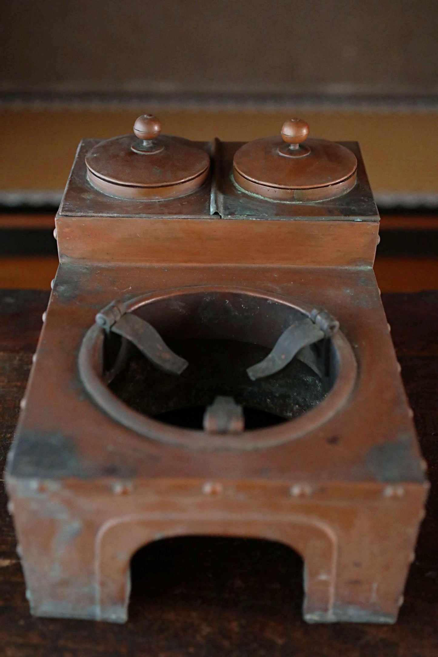 An old, rusted metal object resembling a small stove or cooking appliance, with two round tops and a circular opening in the center.
