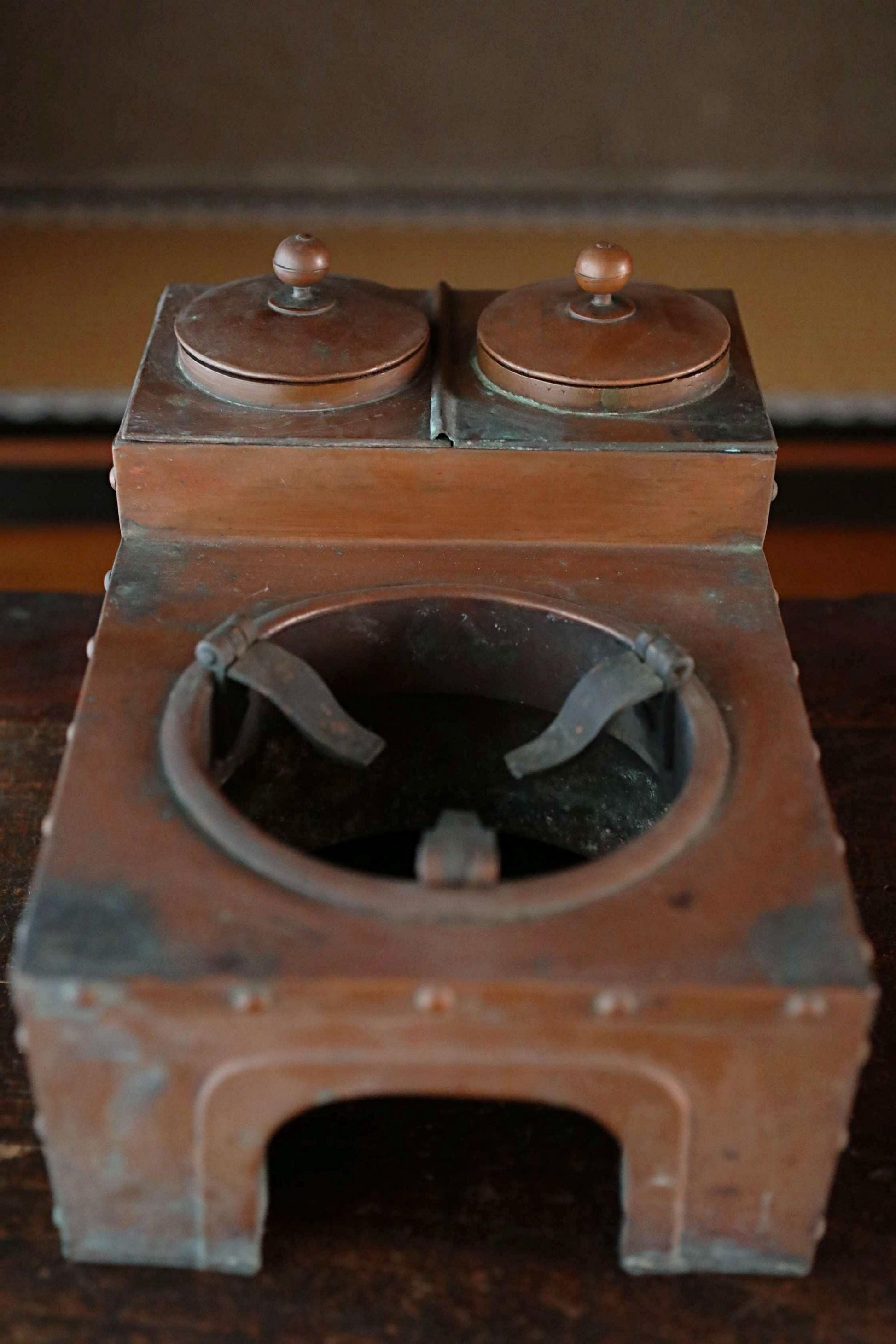 An old, rusted metal object resembling a small stove or cooking appliance, with two round tops and a circular opening in the center.