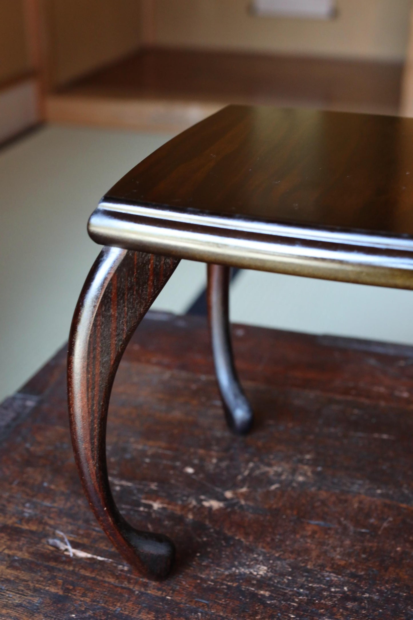A close-up view of a dark wooden table leg with a curved design, resting on a wooden surface.