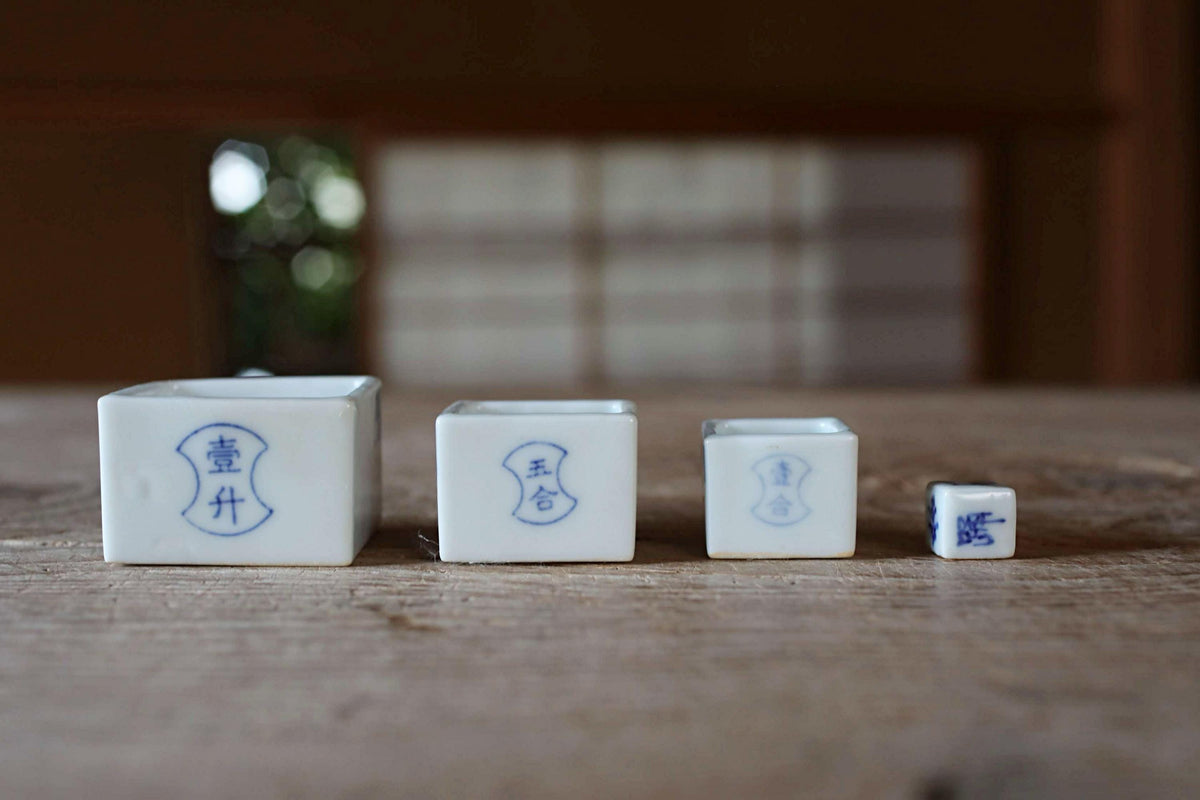 Three small white ceramic cups with blue Chinese characters on them, arranged on a wooden surface.