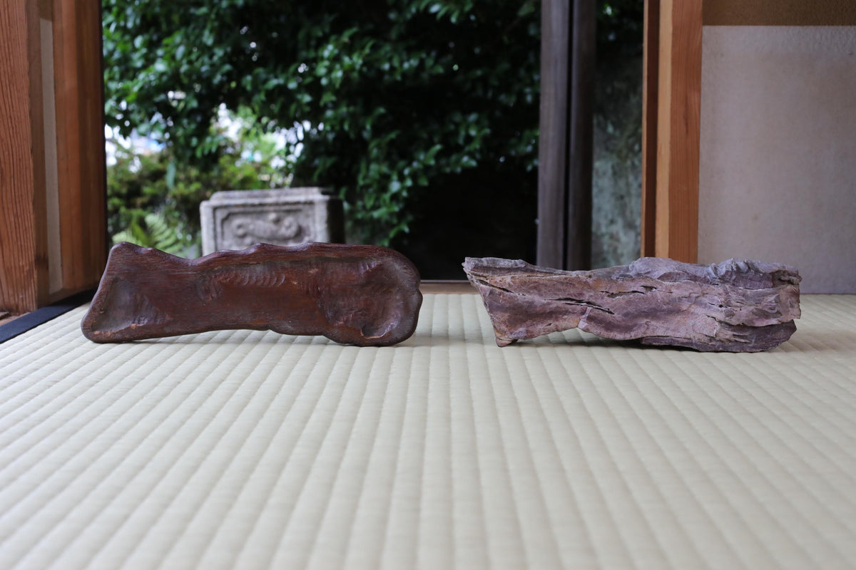 Two large rocks, one brown and one purple, are placed on a white surface, with a wooden structure visible in the background.