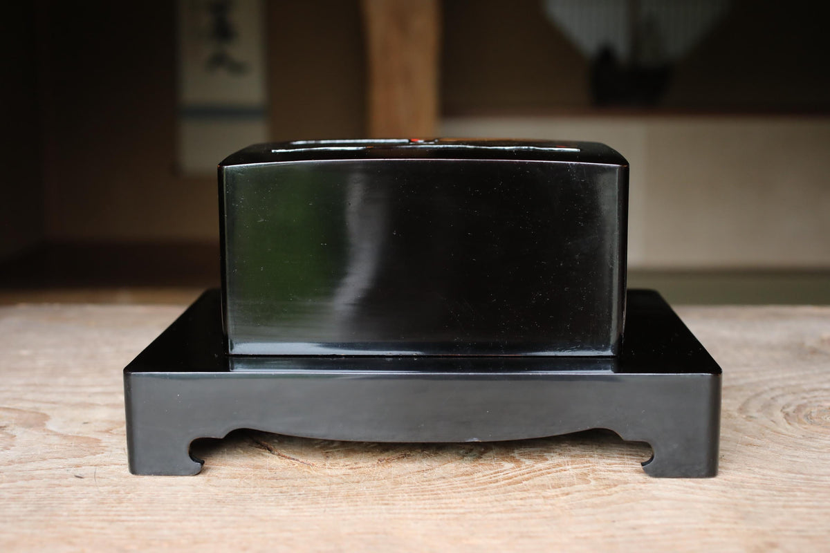 A black rectangular box sits on a wooden surface, with a blurred background.