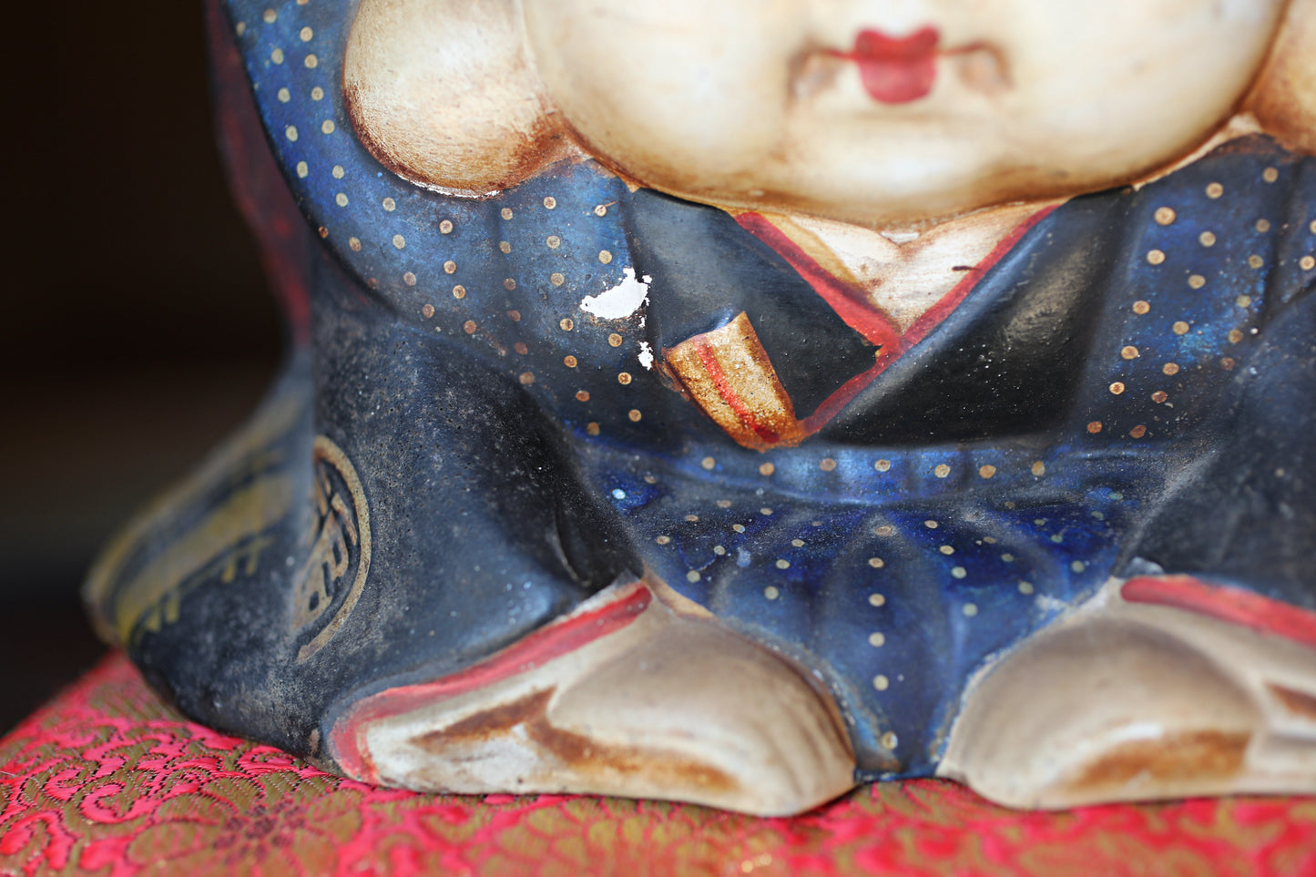 A close-up view of a figurine or sculpture with a blue and red patterned outfit, sitting on a red and gold fabric surface.